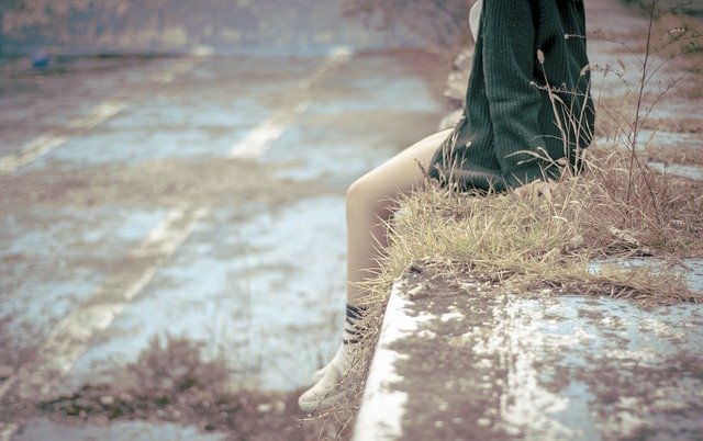 Žena v zelenom svetri sedí na betónovom múriku so spustenými holými nohami.jpg