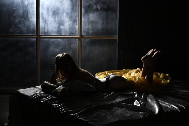 Nahá žena v čiernych erotických tango nohavičkách leží na posteli v tme.jpg